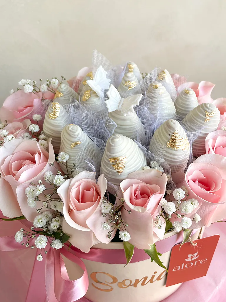 Detalle de fresas bañadas en chocolate blanco con mariposas y rosas rosadas