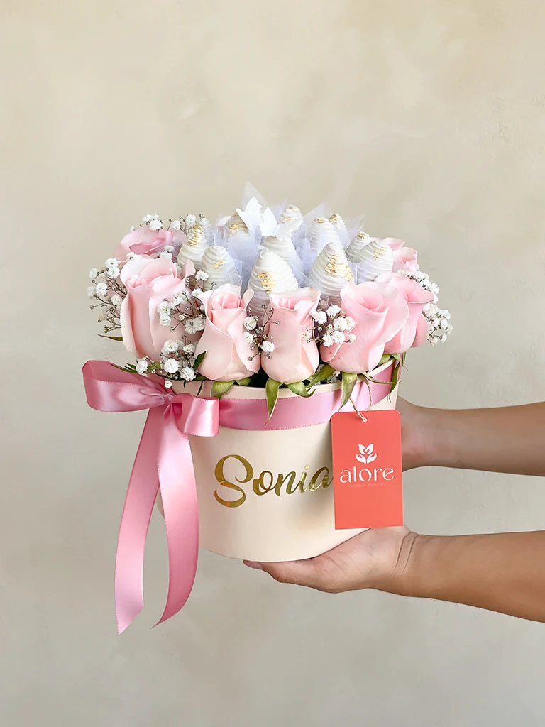 Caja personalizada con rosas rosadas y fresas bañadas en chocolate blanco sostenida en la mano