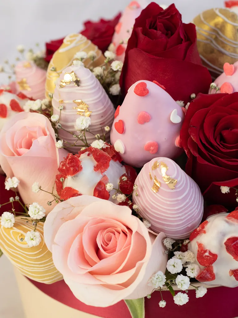 Detalle de fresas bañadas en chocolate rosado y dorado con rosas rojas y palo rosa