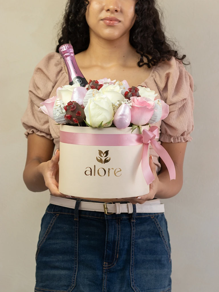 Mujer sosteniendo caja Alore con rosas, fresas bañadas en chocolate y espumante