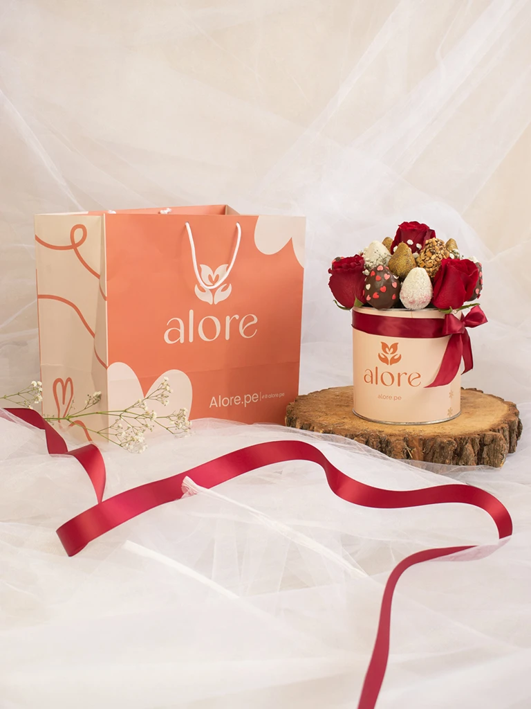 Caja de rosas rojas y fresas bañadas en chocolate junto a bolsa de regalo Alore