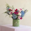 arreglo floral en caja verde con flores azules , rosadas y blancas