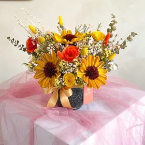 Girasoles eternos con rosas naranjas y flores secas en maceta con lazo dorado
