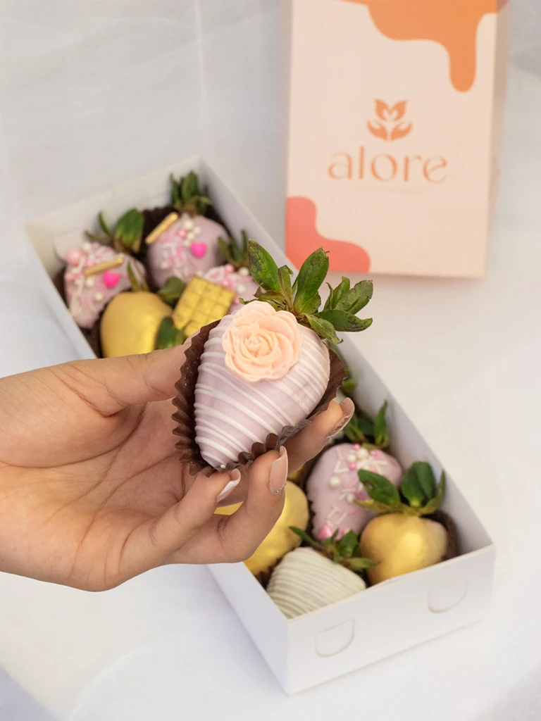 Mano sosteniendo fresa bañada en chocolate blanco con rosa de chocolate