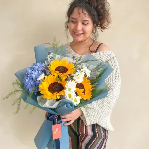 Ramo pequeño de girasoles, hortensia azul y margaritas en papel azul