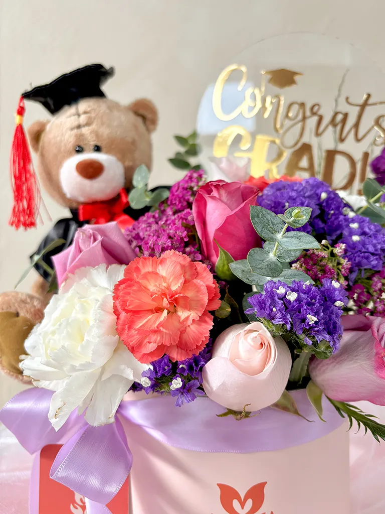 Detalle de osito graduado con rosas, claveles y statice morado y topper "Congrats Grad"