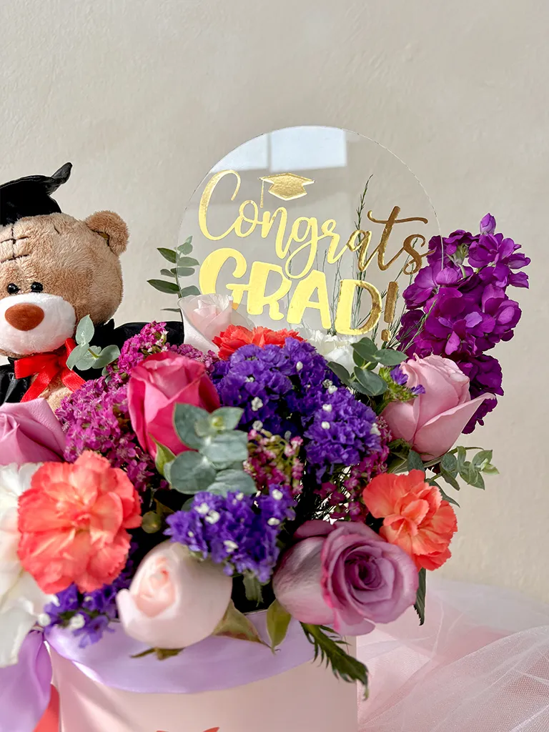 Arreglo de rosas, claveles y flores moradas con osito graduado y topper de graduación