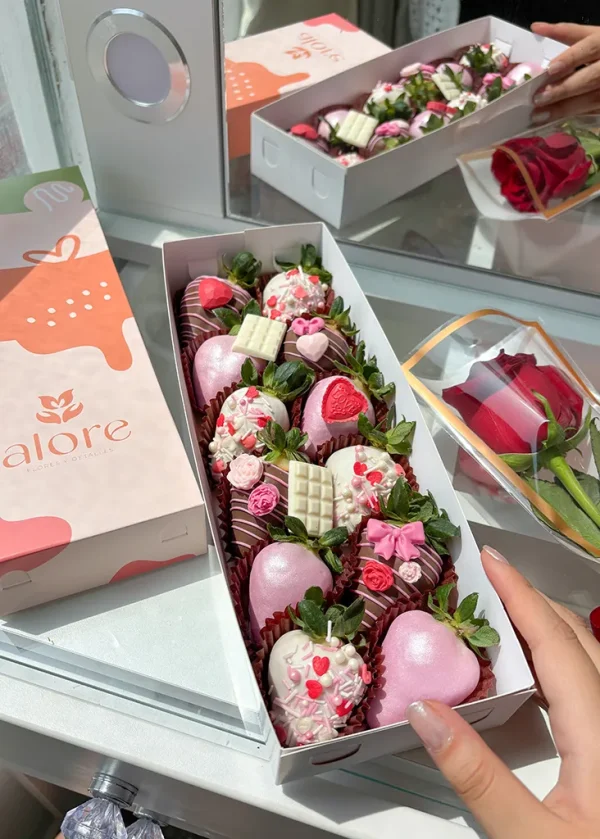 Caja larga con 12 fresas con chocolate y 1 rosa roja en un tocador