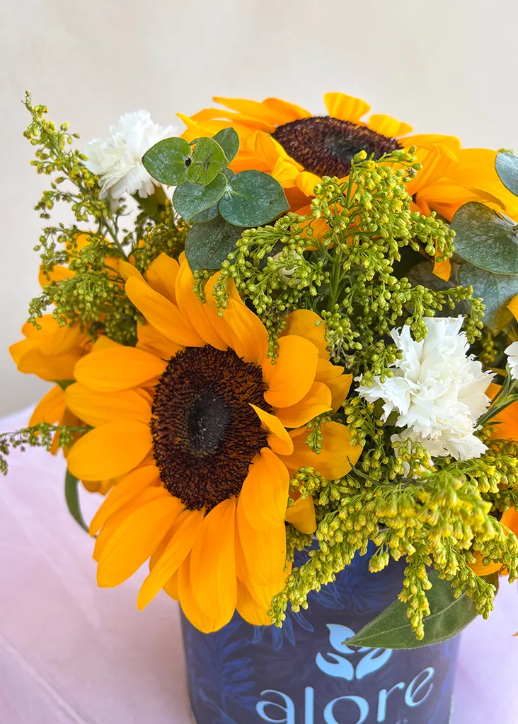 Detalle de girasoles, solidago y flores blancas en caja azul Alore