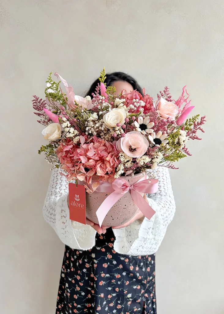 modelo con una maceta de flores preservadas rosada