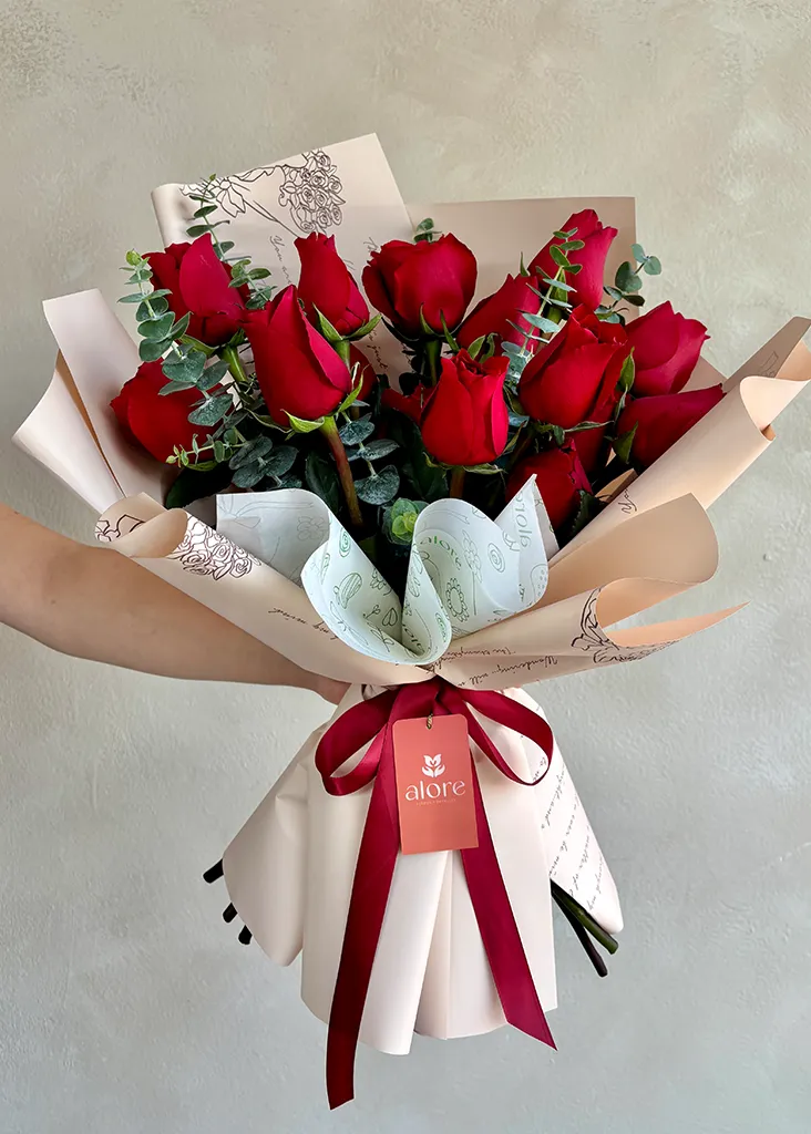 Ramo coreano de rosas rojas con eucalipto y lazo guinda sostenido en la mano
