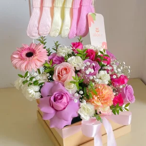 Arreglo de rosas y gerberas en caja con medias de bebé para nacimiento