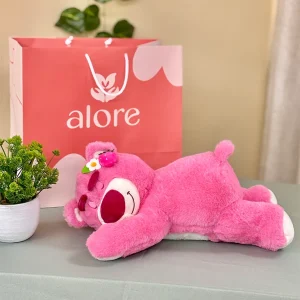Peluche Lotso, oso rosado de Toy Story, echado junto a bolsa de regalo Alore