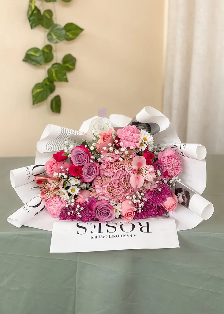 Ramo de rosas y claveles rosados en papel periódico "Roses" sobre mesa