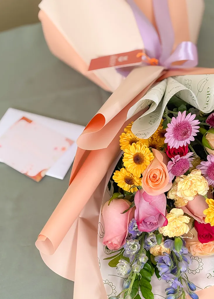 Ramo de rosas, gerberas y flores de colores en papel durazno con tarjeta