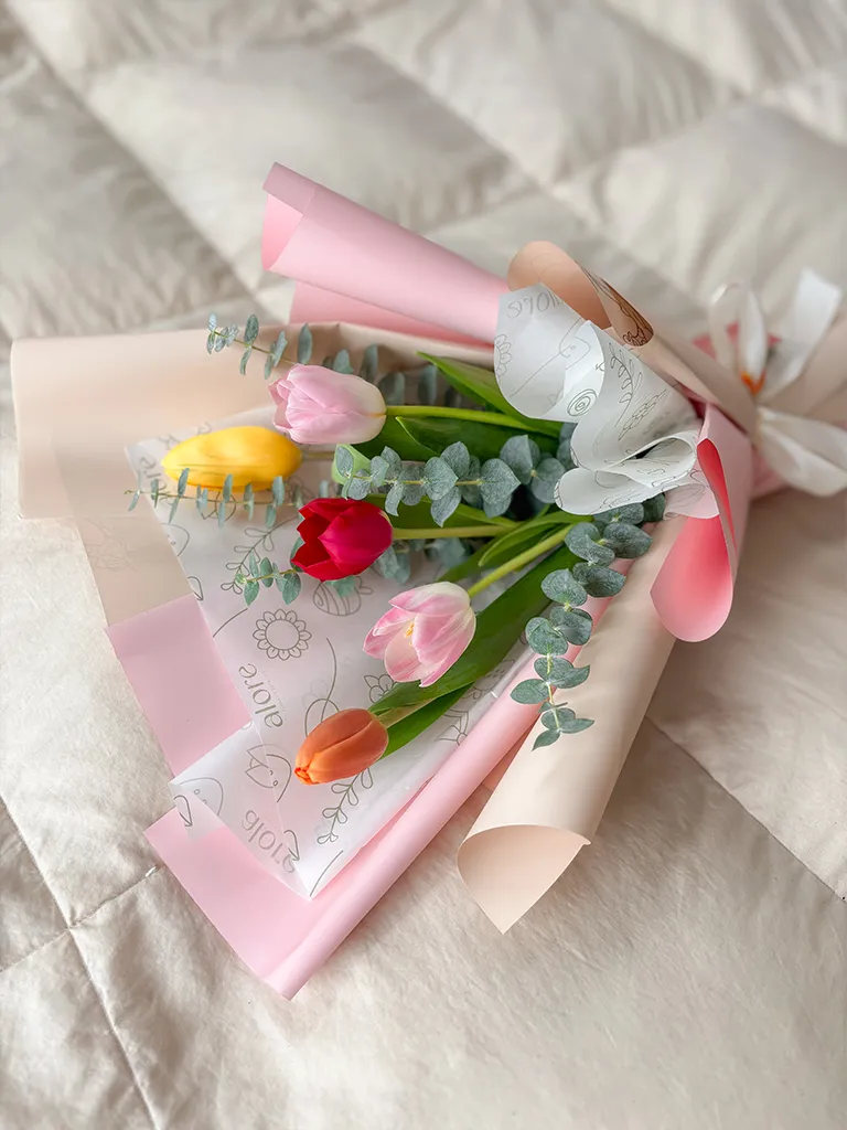 Ramo de tulipanes de colores en papel rosado sobre cama