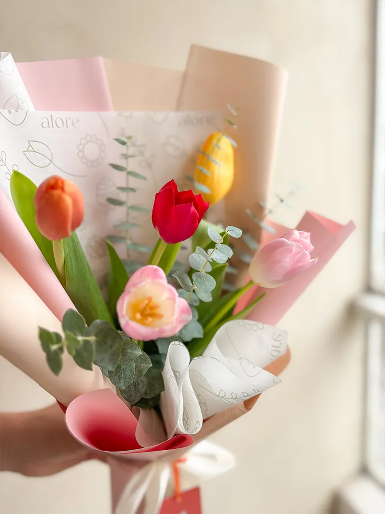 Ramo de tulipanes de colores y eucalipto sostenido en la mano