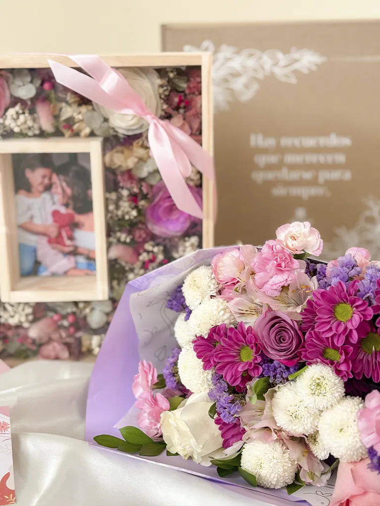 Cuadro de flores eternas con foto junto a ramo de flores rosadas, lilas y blancas